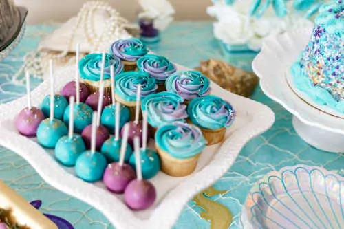 blue and purple cupcakes and cake pops on a party table
