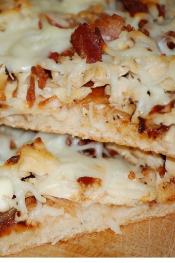 Two thick slices of pizza topped with shredded chicken, crispy bacon, melted mozzarella cheese, and barbecue sauce on a wooden surface.