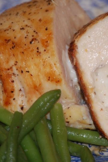 Roasted chicken breast sliced to show a cheesy filling, served alongside crisp cooked green beans on a patterned blue plate