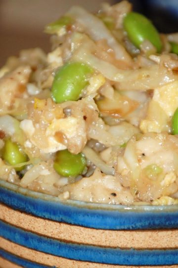 Bowl of stir-fried chicken, scrambled eggs, shredded cabbage, and bright green edamame in a savory rice mixture, served in a striped blue and tan bowl.