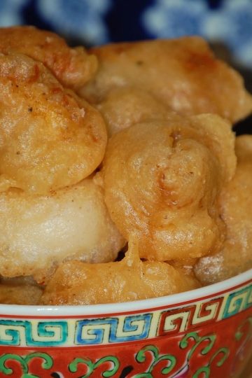 Colorful patterned bowl filled with golden, crispy fried chicken fritters stacked high against a blue patterned background.