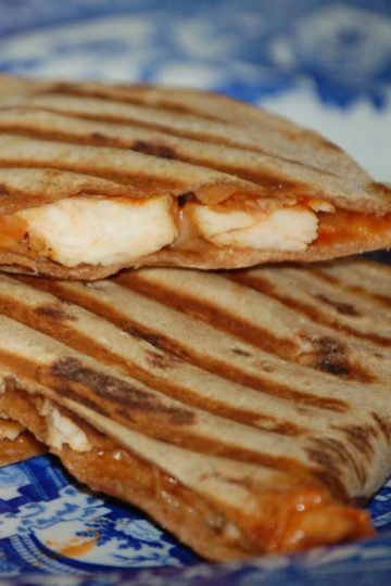 Grilled quesadillas filled with slices of chicken and melted cheese, with golden grill marks, served on a blue patterned plate.