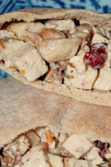 Pita bread pockets filled with a creamy chicken salad mixture, including dried cranberries and chopped nuts, served on a blue patterned plate.