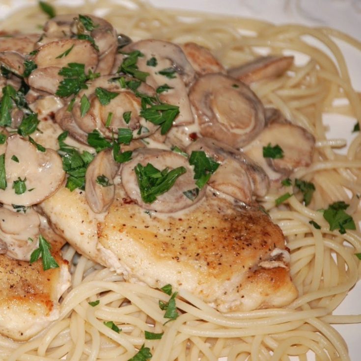Pan-seared chicken breasts topped with creamy mushroom sauce and fresh parsley, served over a bed of spaghetti noodles.