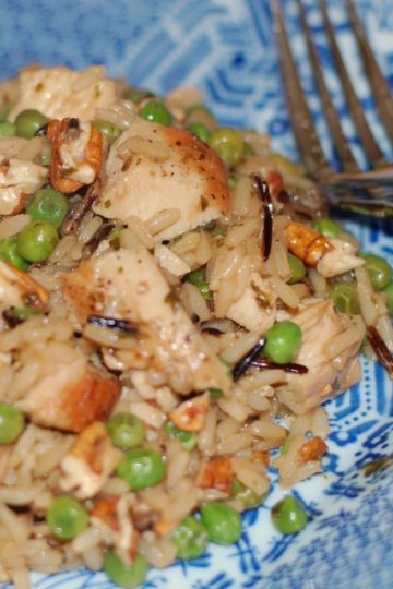 Plate of wild rice and white rice mixed with chunks of chicken, green peas, and chopped nuts, served with a fork on a blue patterned plate.