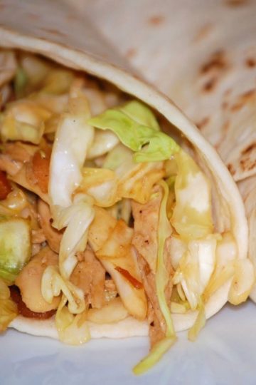 Two soft tortillas filled with shredded chicken, cooked cabbage, carrots, and a savory sauce, placed on a white background.