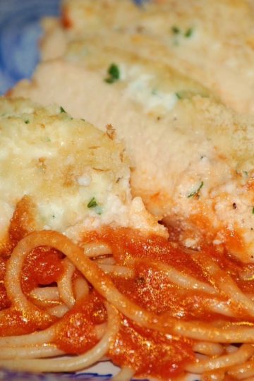 Baked chicken breasts topped with ricotta and parmesan cheese, served with spaghetti noodles and marinara sauce on a blue patterned plate.