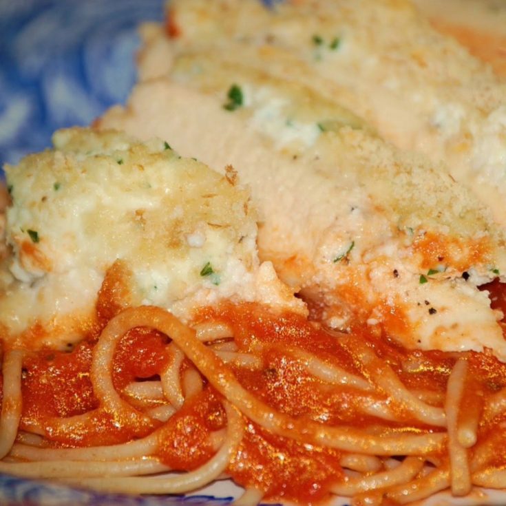 Baked chicken breasts topped with ricotta and parmesan cheese, served with spaghetti noodles and marinara sauce on a blue patterned plate.
