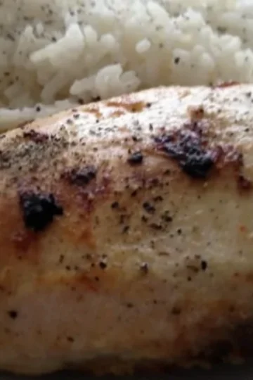 Seasoned and baked chicken breast with visible black pepper, served alongside a portion of white rice sprinkled with black pepper on a white plate.